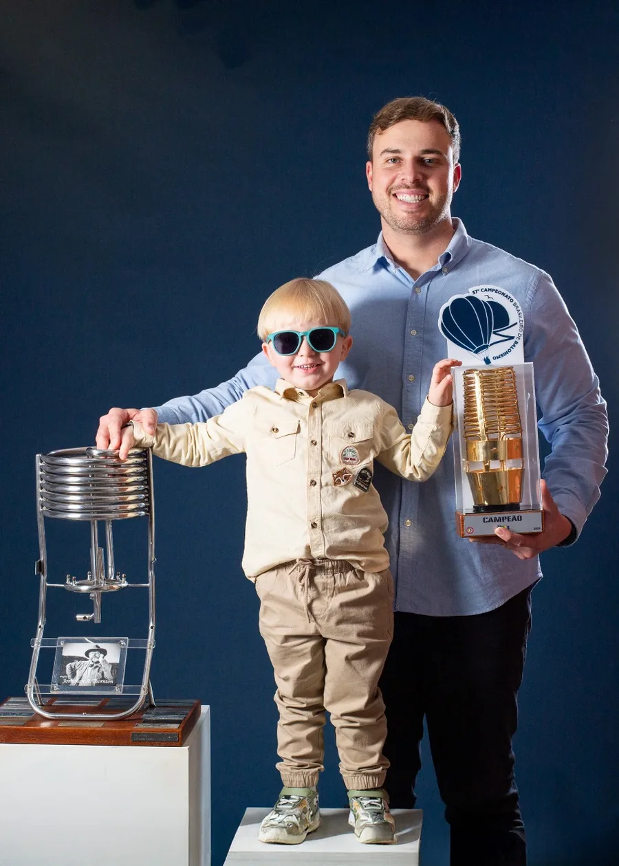 João Vitor Justo com o filho, segurando o troféu de campeão do 37º Campeonato Brasileiro de Balonismo