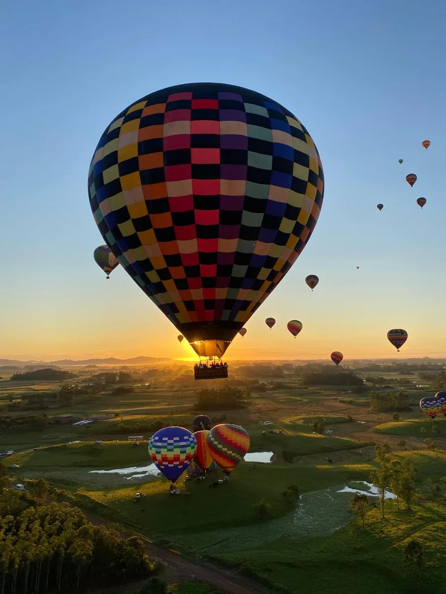 Vista aérea de vários balões coloridos sobrevoando o campo ao nascer do sol