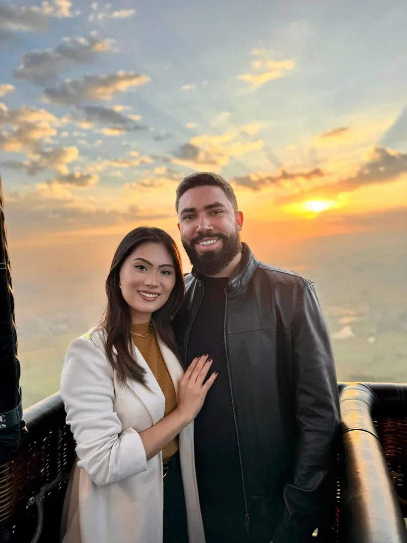 Casal abraçado no cesto com o sol nascendo sobre os campos