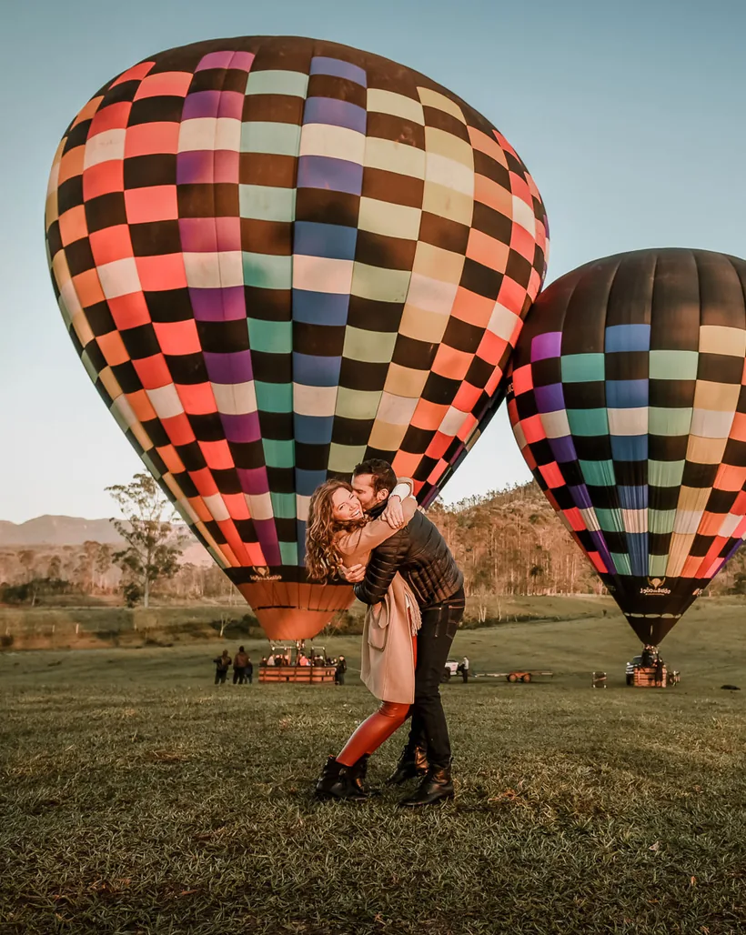 Casal se beijando em frente a dois balões do João do Balão prontos para decolar
