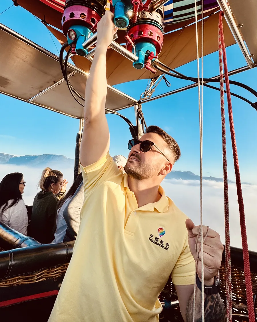 O piloto Peretto operando o maçarico do balão durante o voo, com o mar de nuvens ao fundo